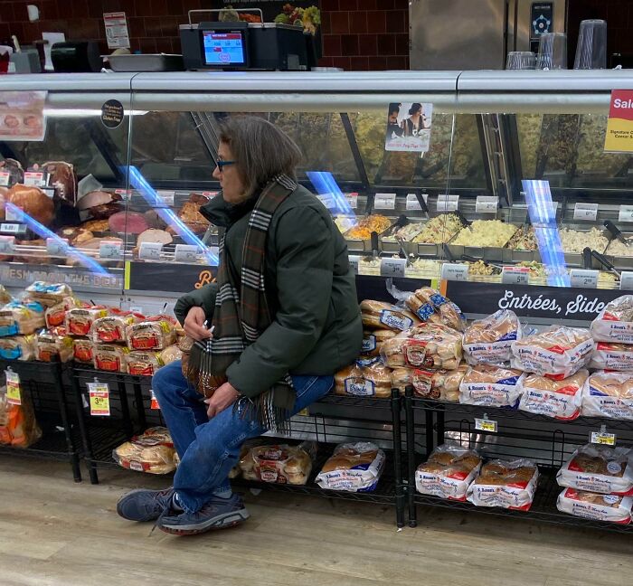 Cliente frustrado sentado en supermercado cerca de pan y charcutería, reflejando historias de empleados con clientes difíciles.