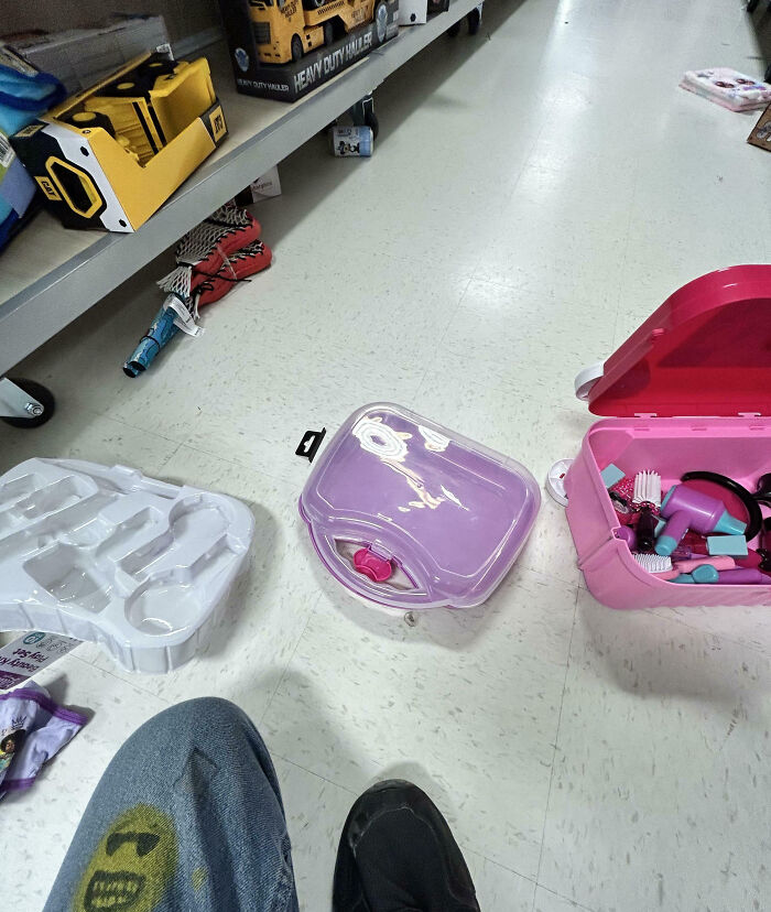 Contenedor rosa abierto con juguetes y herramientas en suelo de tienda, empleados frustrados con clientes ignorantes y tontos