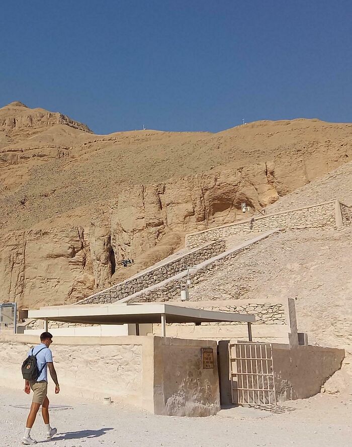 Un hombre caminando junto a una estructura en un sitio arqueológico bajo un cielo despejado.
