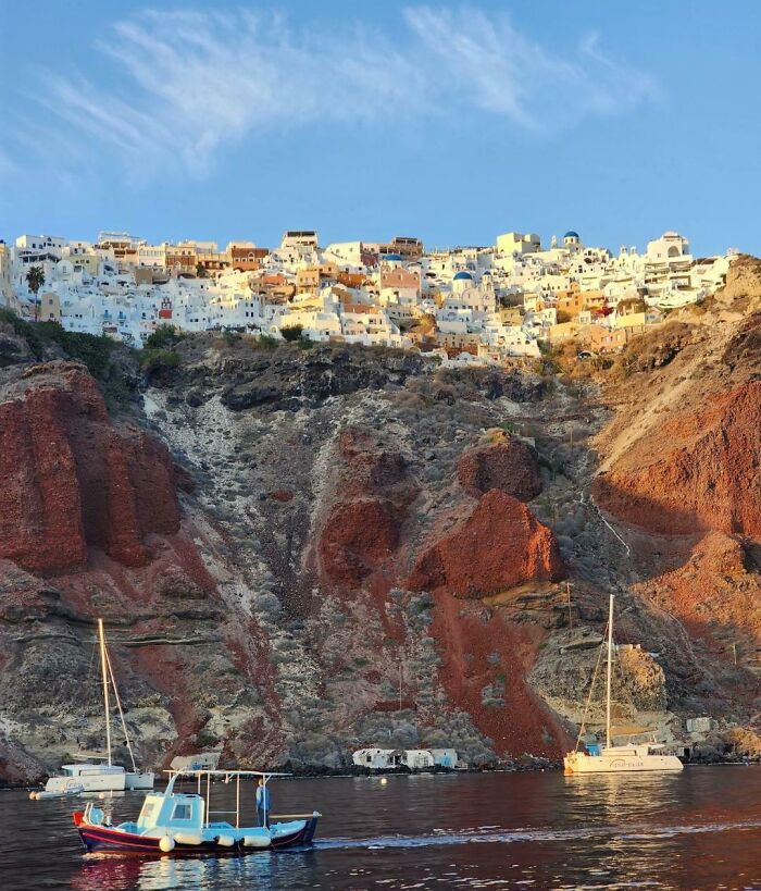 Vista de un lugar conocido con casas blancas en un acantilado, bote y velero en el mar.