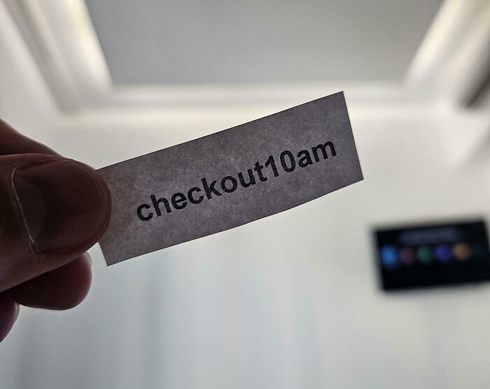"Nota divertida y pasivo-agresiva: 'checkout 10am', sostenida con una mano en un entorno minimalista."