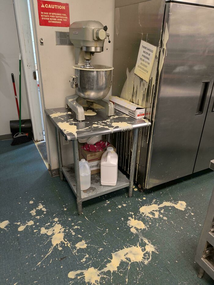 Batidora industrial derrama masa en cocina, mostrando un día difícil en el trabajo.