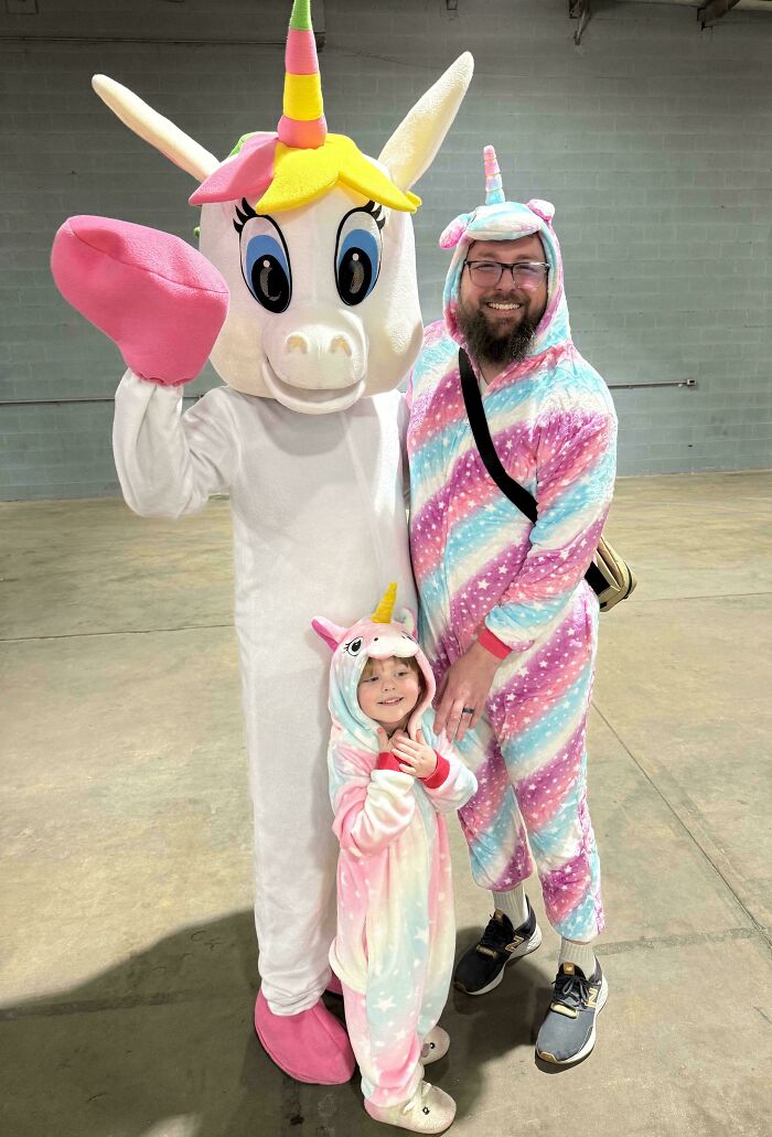 Padre e hijo vestidos con disfraces de unicornio posando junto a persona con disfraz de unicornio en momento familiar divertido.