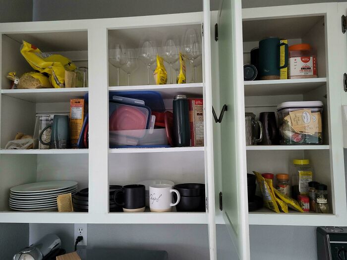 Gabinete de cocina desorganizado con platos, vasos y alimentos.