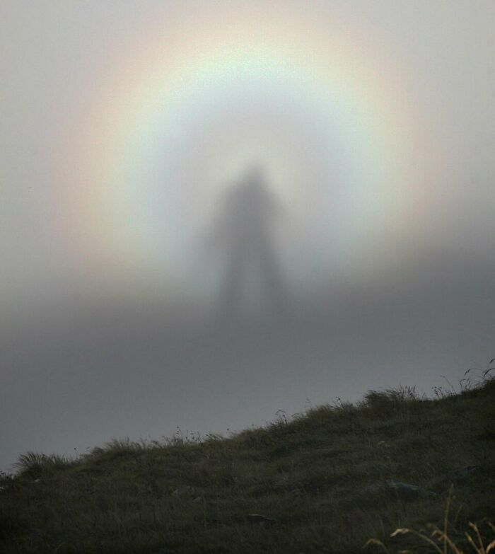 Silueta surrealista de una figura rodeada por un arco iris en la niebla.