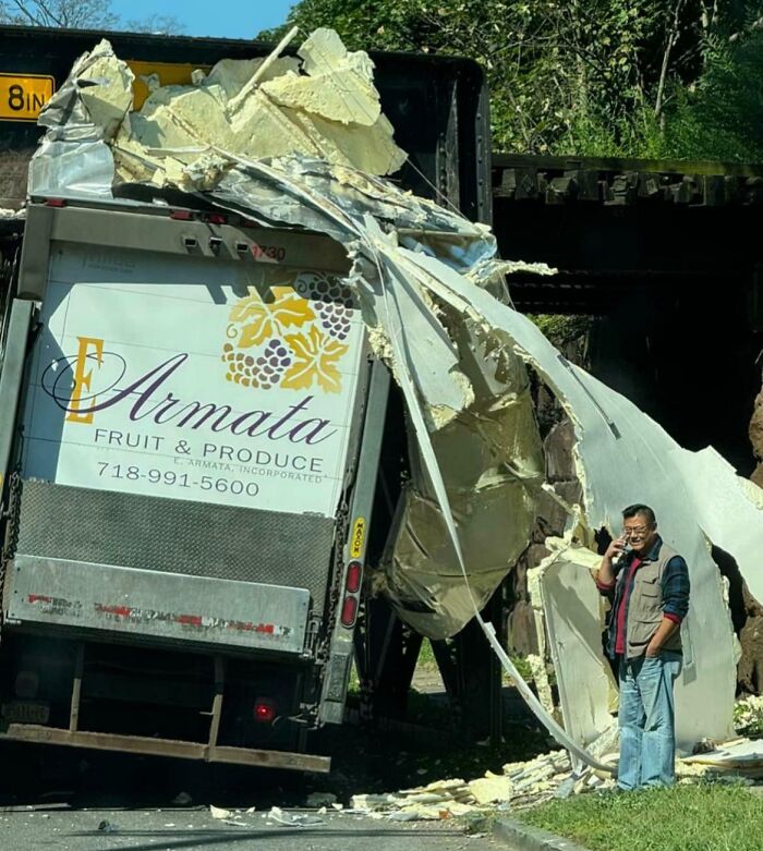 Camión de frutas dañado bajo un puente, conductor hablando por teléfono; día difícil en el trabajo.