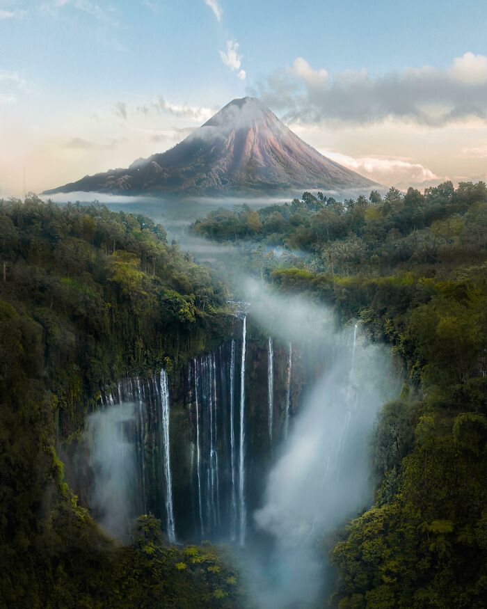 Montaña y cascada en paisaje surreal rodeado de niebla y vegetación exuberante.