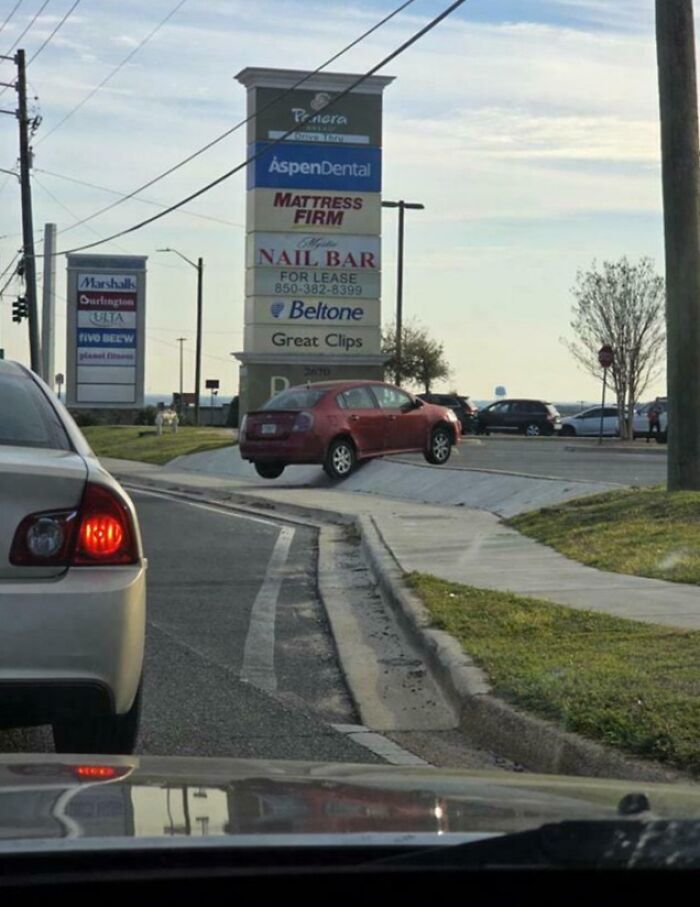 Coche rojo mal estacionado en una acera frente a una plaza comercial, ejemplo de errores compartidos en internet.