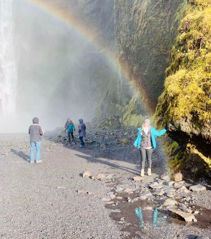 Personas bajo cascada y arcoíris, escena surreal en la naturaleza.