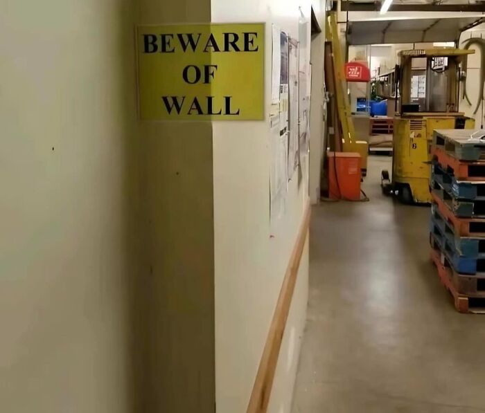 Aviso legal divertido en bodega industrial con señal de precaución sobre la pared para evitar accidentes laborales.