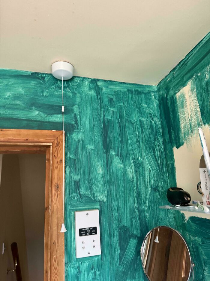 Pared verde mal pintada con interruptor blanco y espejo, ejemplo de reparación empeorada.