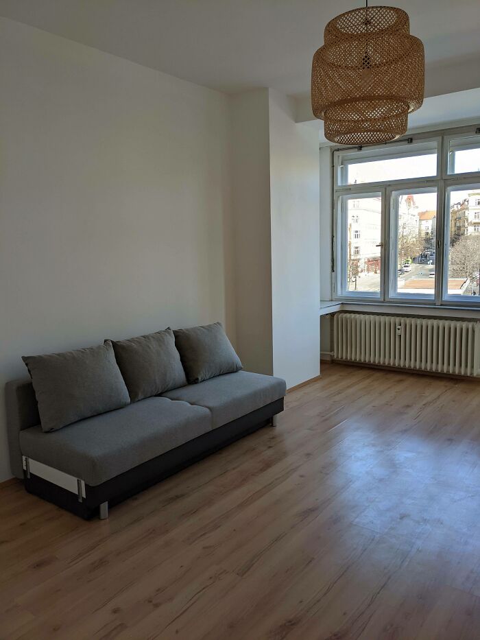 Sofá gris en una sala minimalista con tendencia de interiorismo poco práctica, lámpara de mimbre y vista al exterior.