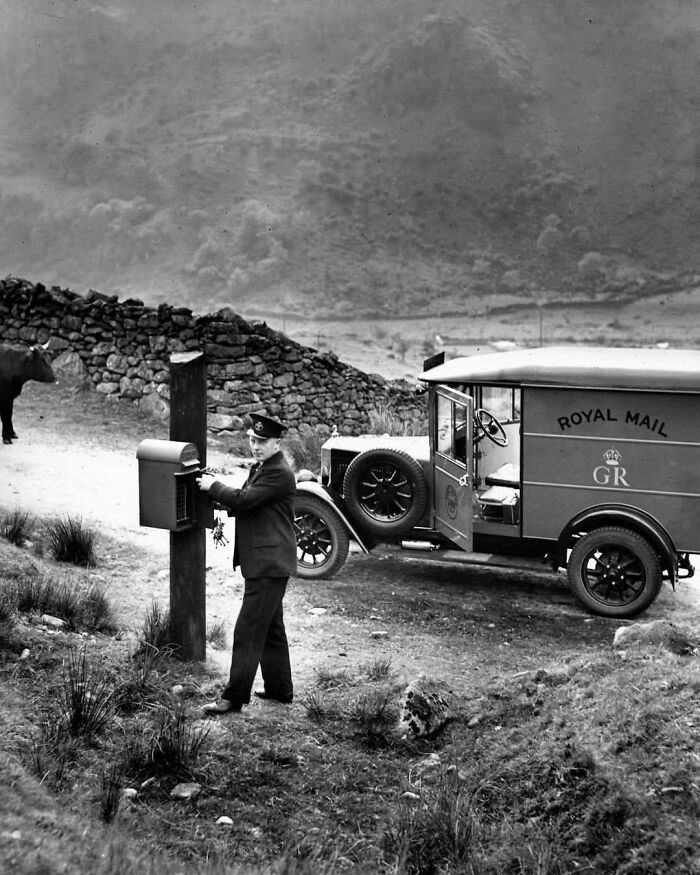 Cartero del Royal Mail colocando cartas en buzón rural, imagen histórica de días pasados.