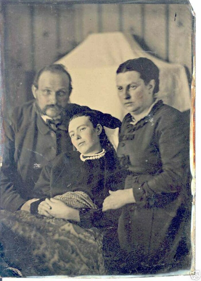 "Retrato inquietante de tres personas en blanco y negro, dos de pie y una recostada en el centro del cuadro."