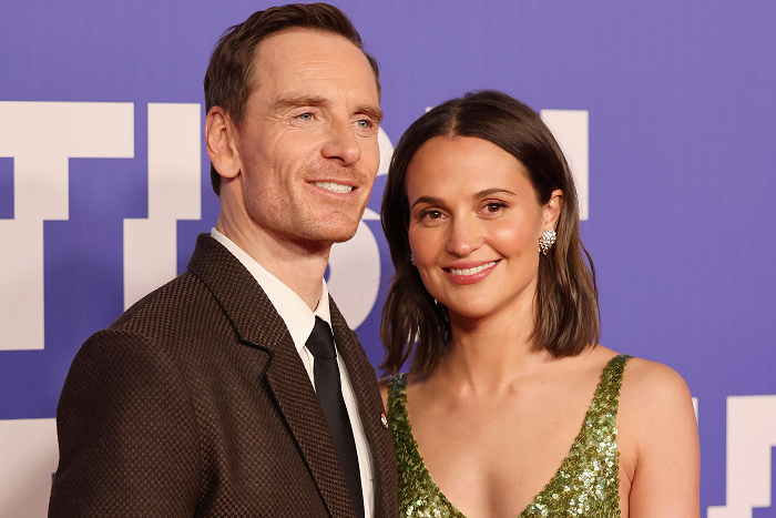 Pareja de celebridades sonriendo en un evento, fondo azul.