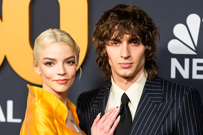 Pareja de celebridades ultra privada en un evento, ella con vestido naranja y él con traje a rayas.
