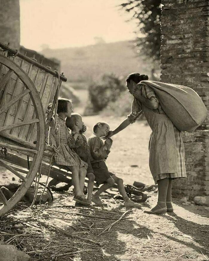 Mujer y niños en una escena rural histórica, junto a un carro de madera, evocando tiempos pasados.