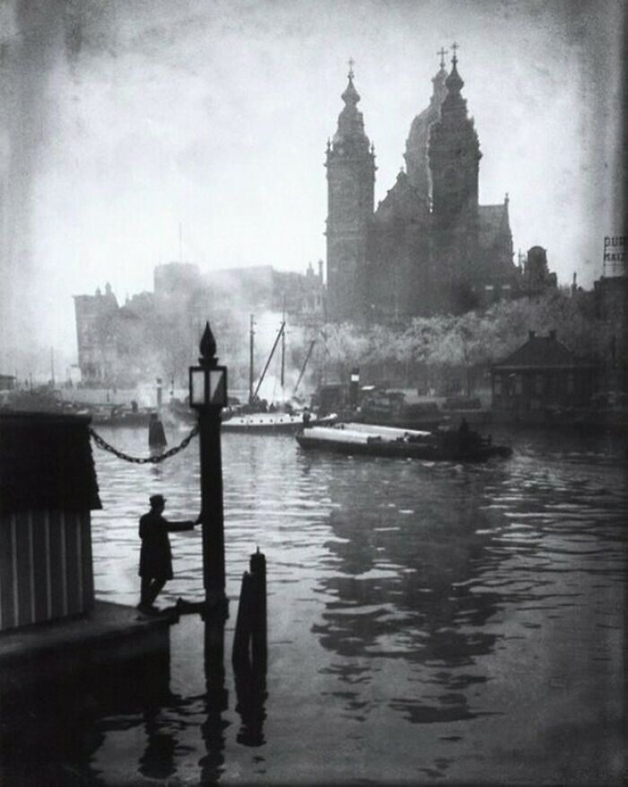Persona junto al agua con un gran edificio al fondo en una antigua foto histórica.