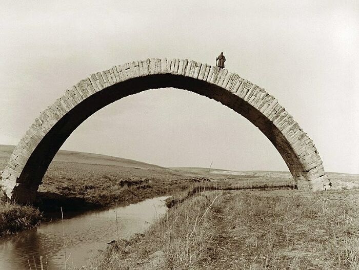 Persona de pie sobre un puente histórico en un paisaje rural, evocando el pasado.