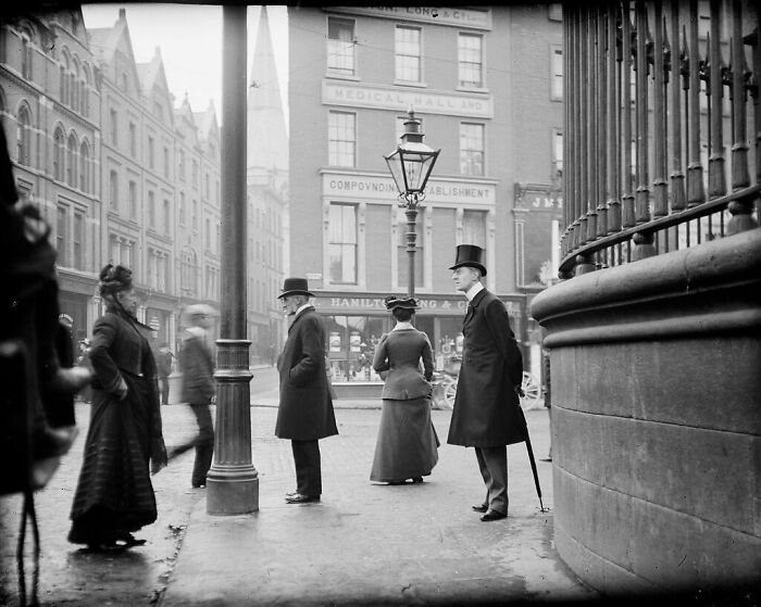 Personas vestidas de época victoriana en una calle histórica, capturando la esencia del pasado.