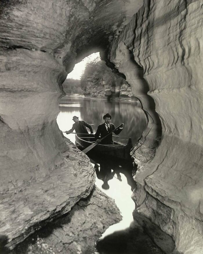 Hombres en un bote de remos a través de una formación rocosa, escena histórica que evoca el pasado.