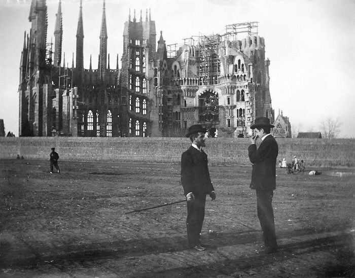 Construcción histórica de la Sagrada Familia en proceso, hombres de pie conversando al frente.