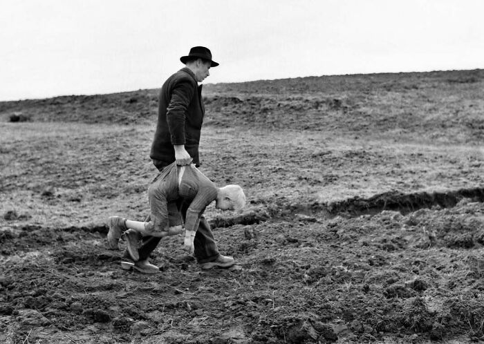 Un hombre con sombrero transporta a un niño por el campo en una escena histórica en blanco y negro.
