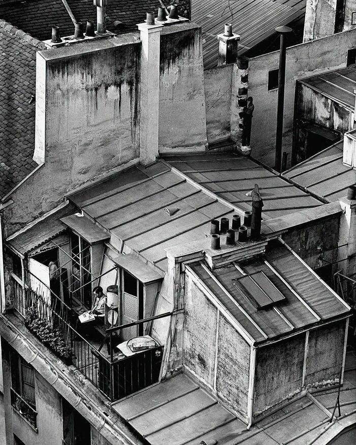 Tejados históricos con una persona leyendo en un balcón, capturando la esencia del pasado urbanístico.