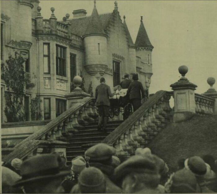 Grupo de personas subiendo unas escaleras con un cochecito frente a un castillo histórico.