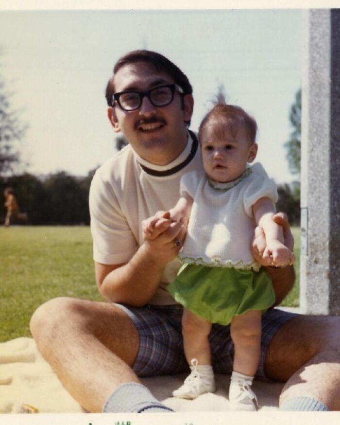 "Foto antigua de un hombre con gafas sosteniendo a un bebé en un parque, mostrando un momento familiar pasado."