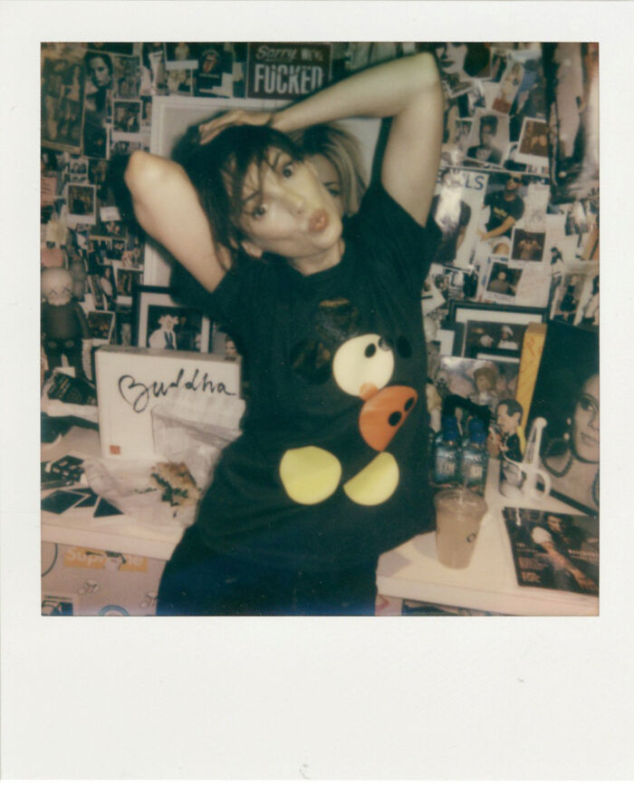 Persona posando en habitación decorada con fotos antiguas y camiseta de diseño retro.