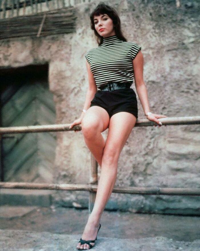 Una mujer con ropa vintage, posando en un entorno urbano antiguo.