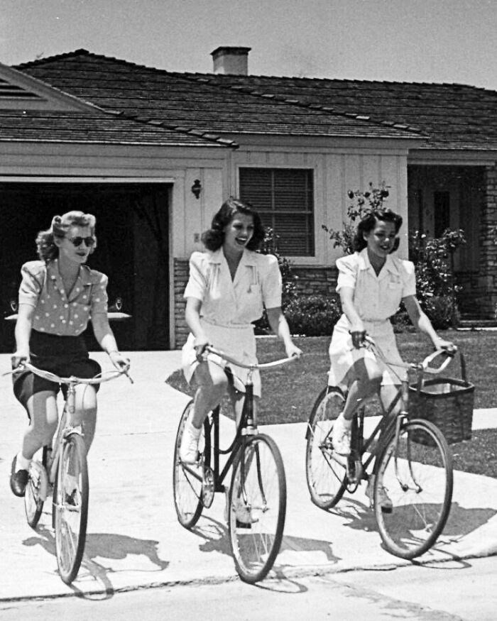 Mujeres en bicicletas antiguas frente a una casa, mostrando cómo ha cambiado la moda con el tiempo.
