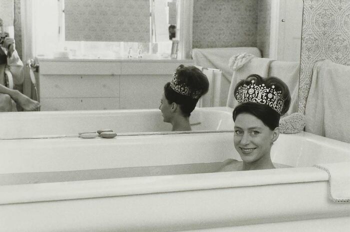 Mujer con corona en una bañera, reflejada en el espejo, evocando cambios en costumbres modernas.