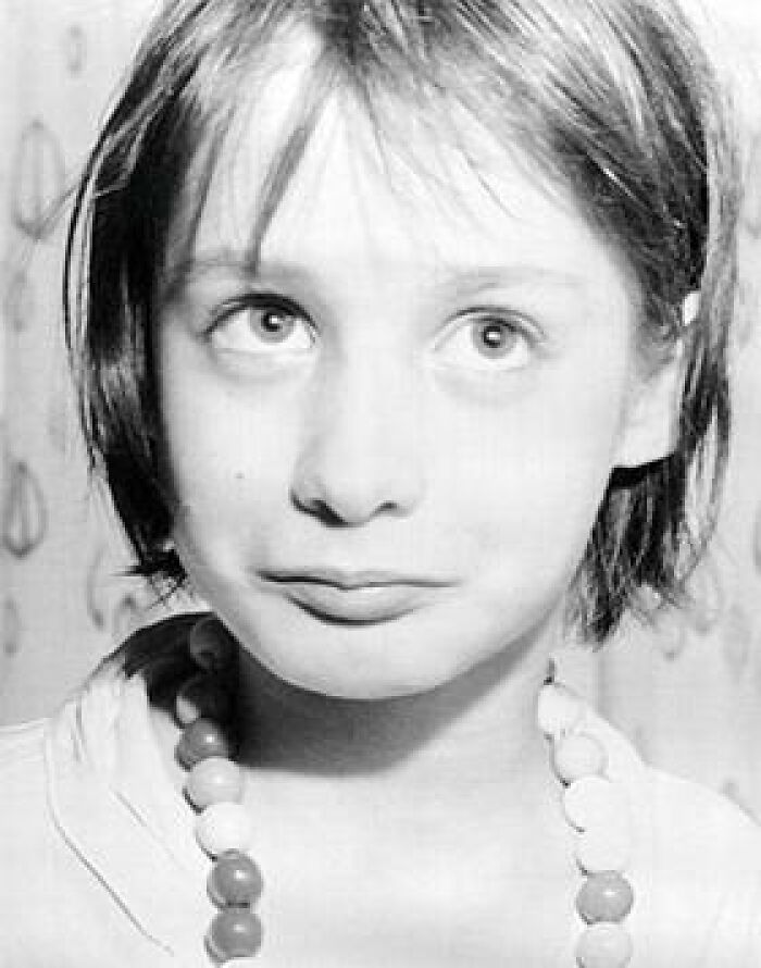 Niña con collar de cuentas grandes, mirada inquietante.