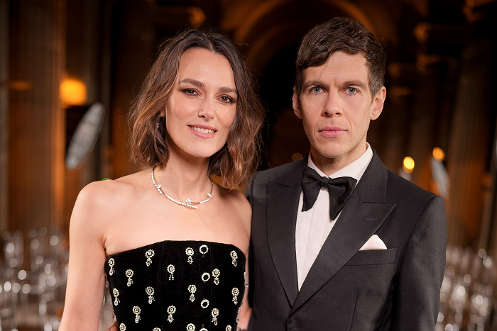 Pareja de celebridades ultra privada posando en un evento elegante, él lleva esmoquin y ella un vestido negro.