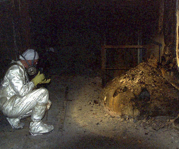 Persona en traje protector observando una formación anormal en una sala oscura, foto inquietante con historia misteriosa.