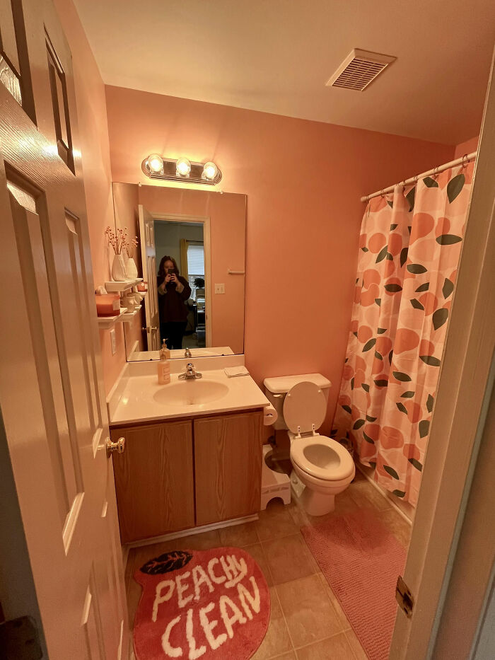 Baño con decoración interiorismo en tonos melocotón, incluyendo cortina y alfombra decorativa.