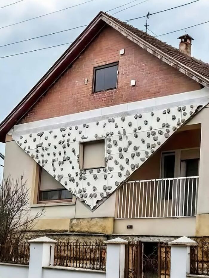 Casa con diseño arquitectónico inusual, fachada triangular cubierta de piedras pequeñas.