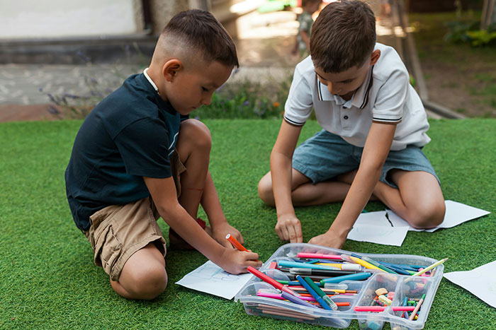 Niños dibujando en el césped, rodeados de crayones, reflejando momentos de infancia.