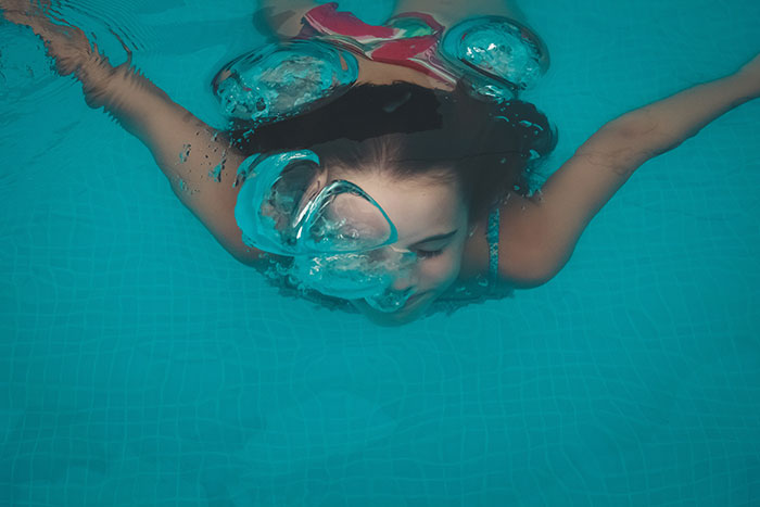 Niña buceando en una piscina, creando burbujas, simbolizando recuerdos infantiles.