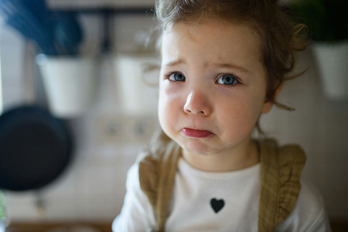 Niña con expresión triste en la cocina, reflejando experiencias de infancia.