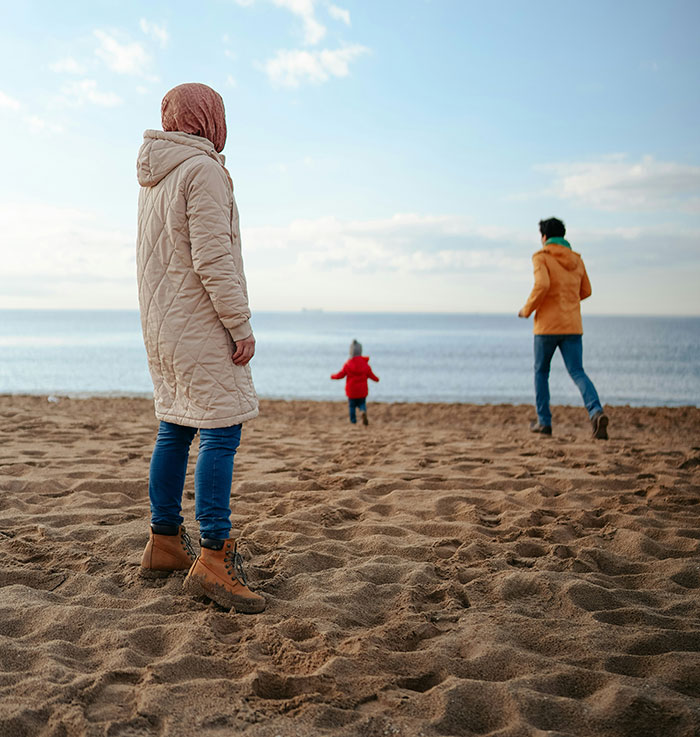 Personas en la playa con abrigos, mirando al mar, un niño caminando hacia el agua.