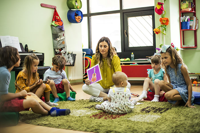 Una maestra en círculo con niños en una guardería, escena de infancia.