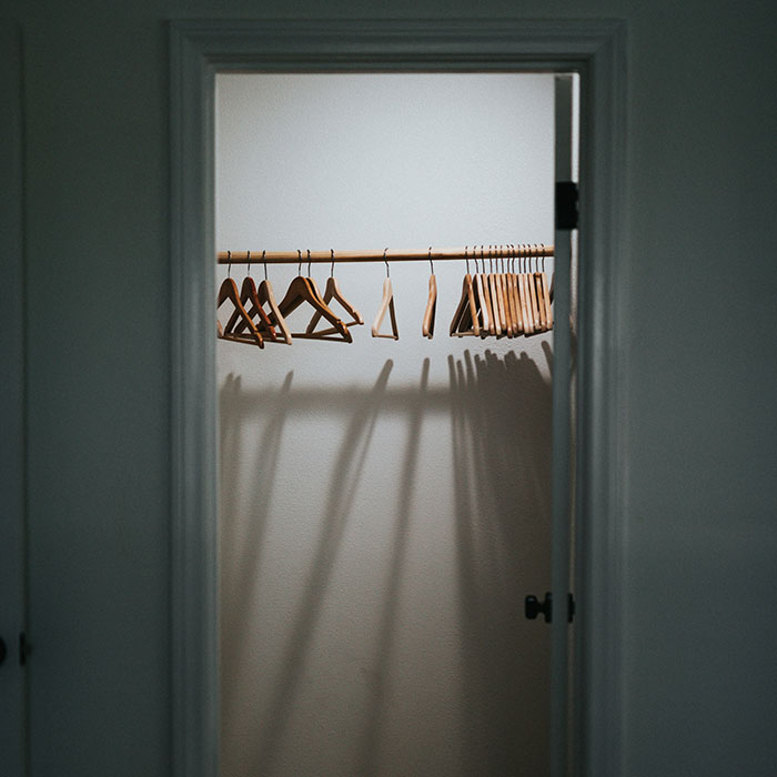 Armario vacío y oscuro con perchas de madera, evocando recuerdos de infancia.