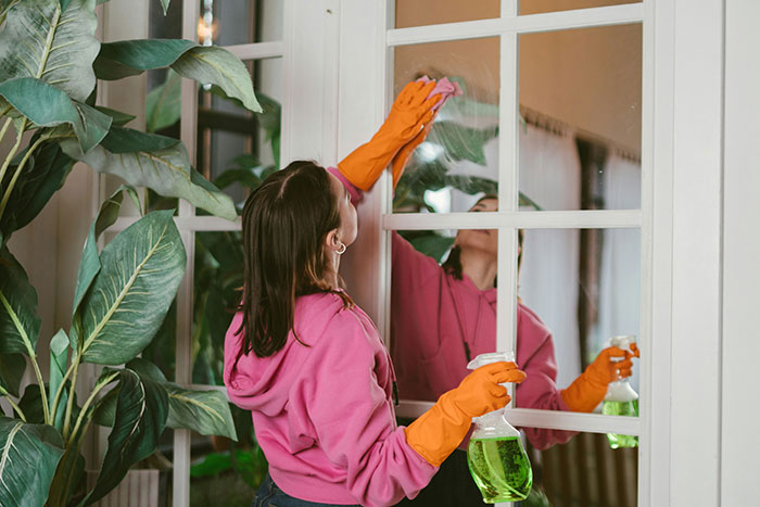 Persona limpiando ventana, lleva guantes naranjas y sudadera rosa, simbolizando recuerdos de infancia.