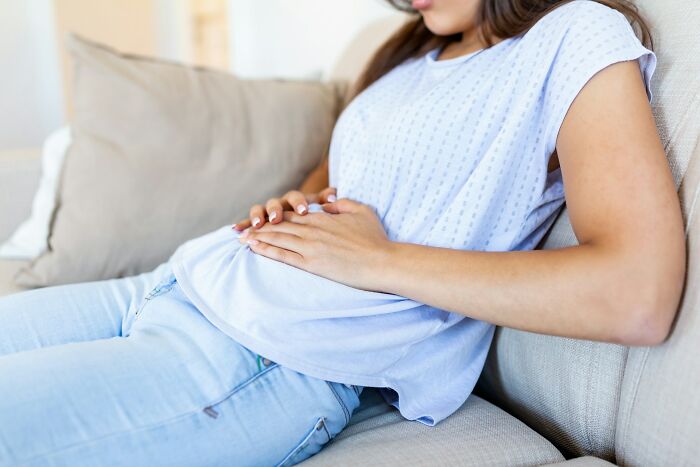 Mujer con malestar estomacal acostada en un sofá, imagen relacionada con datos útiles para salvar vidas.