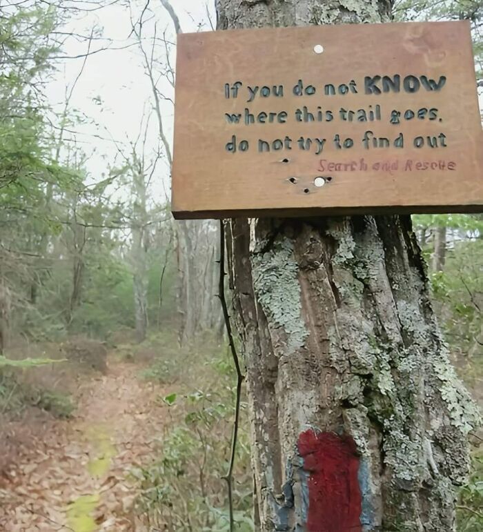 Aviso legal divertido en sendero señalando no intentar seguir si no se conoce el camino para evitar demandas.