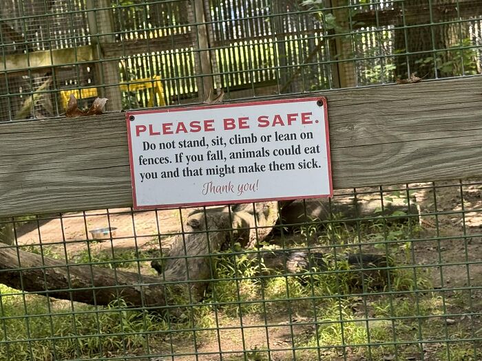 Aviso legal divertido en cerca de parque con advertencia de seguridad sobre animales y posibles demandas.