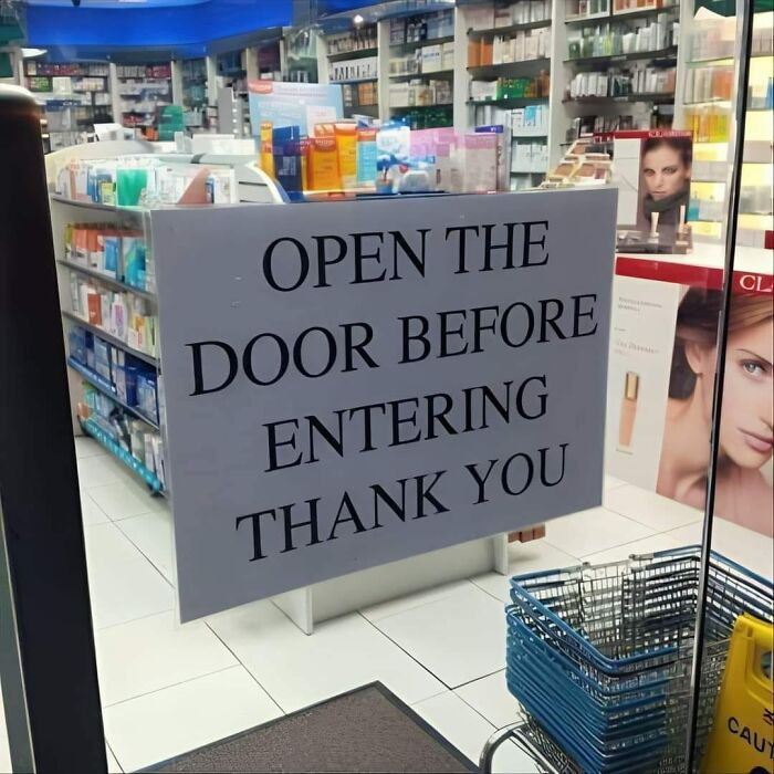 Aviso divertido y legal en farmacia que indica abrir la puerta antes de entrar, ejemplo de aviso tras una demanda.
